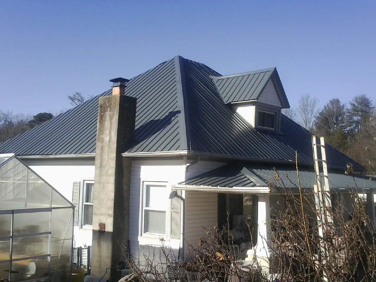 Dark blue standing seam metal roof on a white farmhouse with dormer — Slate & Tile Roof Repair by Roofing Brothers in Iron Ridge