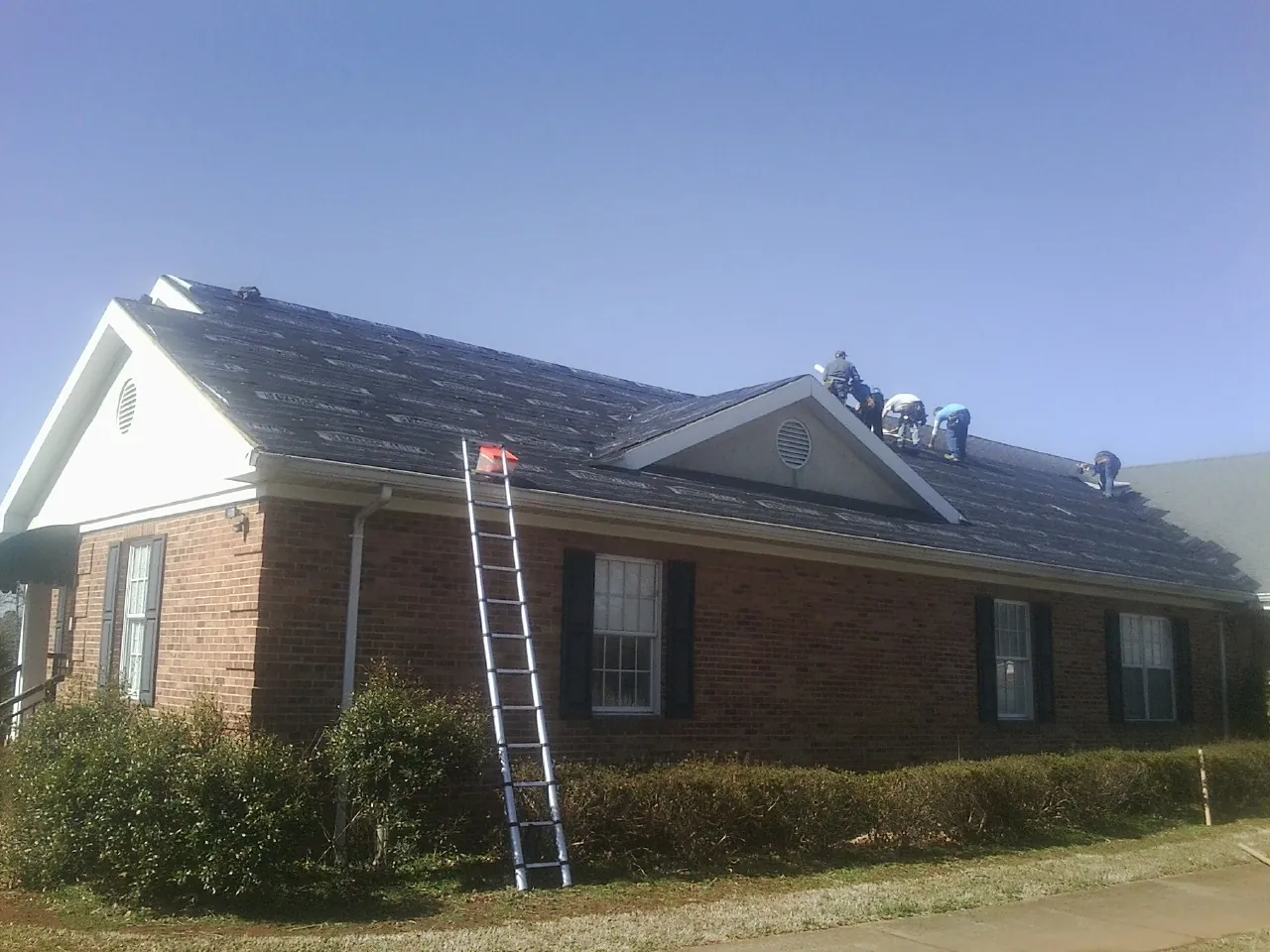 Crew tearing shingles off a brick ranch roof with a ladder set — Emergency Roof Repair work by our crew in Iron Ridge