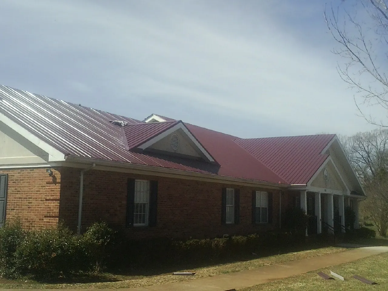Red metal roof with gabled entries on a long brick building, from a Hail Damage Roof Repair job in Iron Ridge