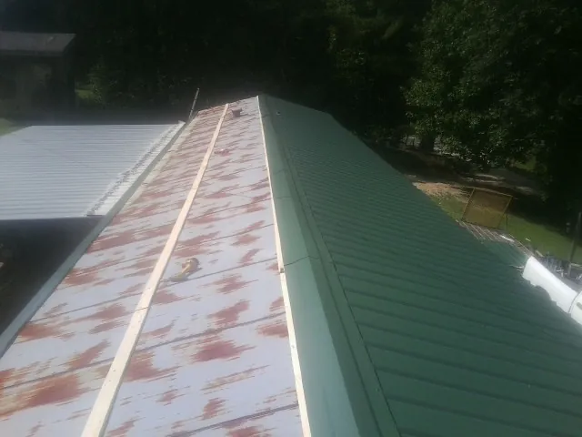Old rusted panels beside newly installed green metal roofing — Wind Damage Roof Repair by Roofing Brothers in Iron Ridge