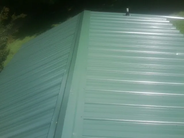 New green metal panels meeting at the ridge of a roof — Flat Roof Repair work by our crew in Iron Ridge