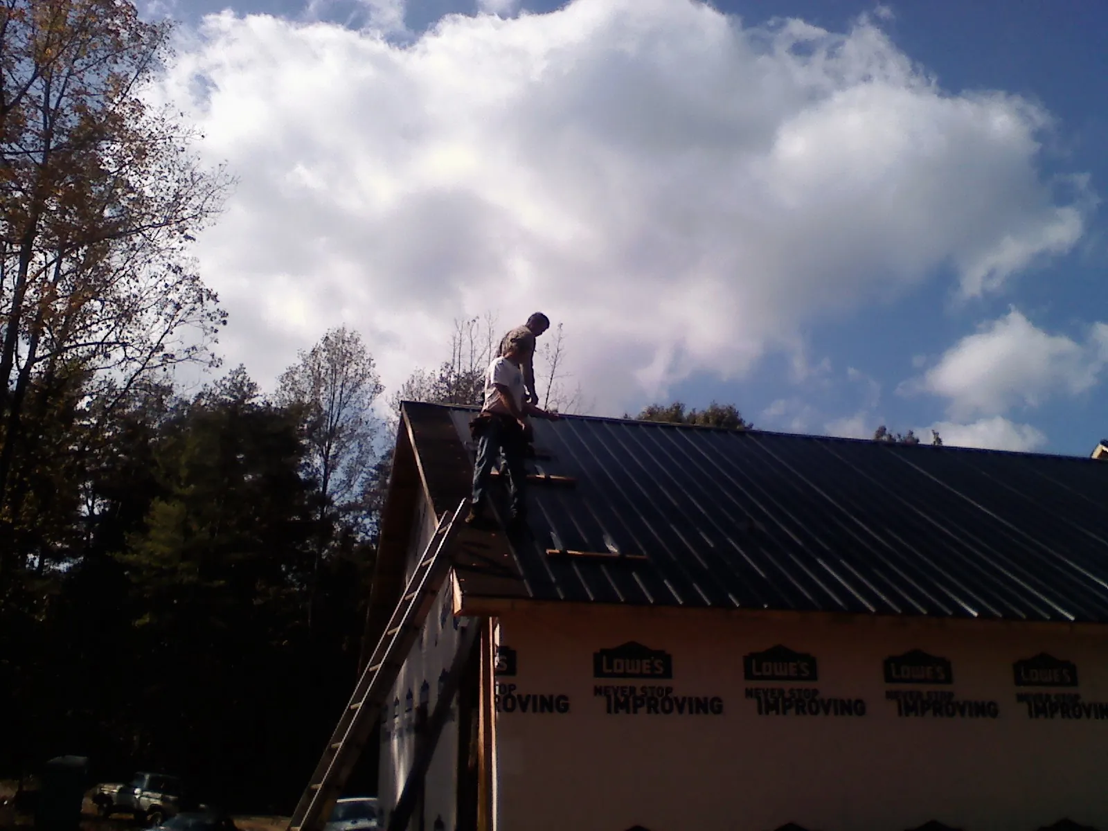 Roofer fastening dark metal panels high against a cloudy sky, from a Roof Inspection job in Iron Ridge