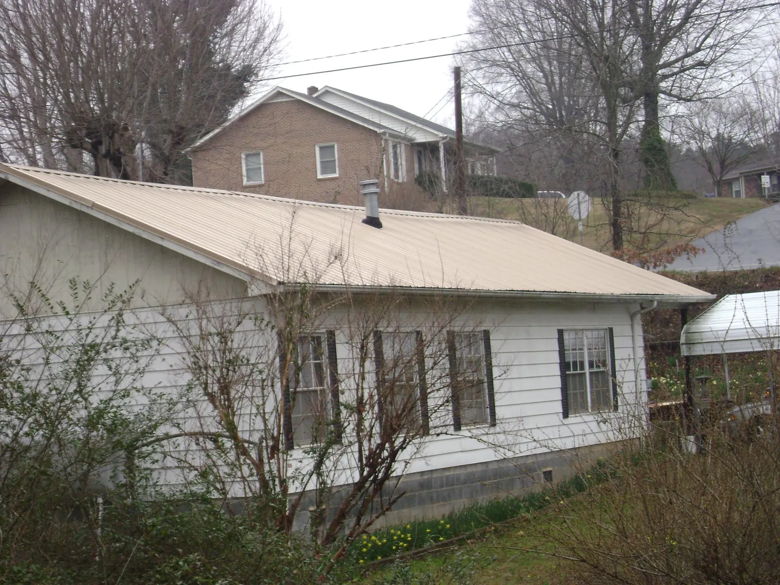 Tan metal roof on a white sided house set into a hillside — Commercial Roofing by Roofing Brothers in Iron Ridge