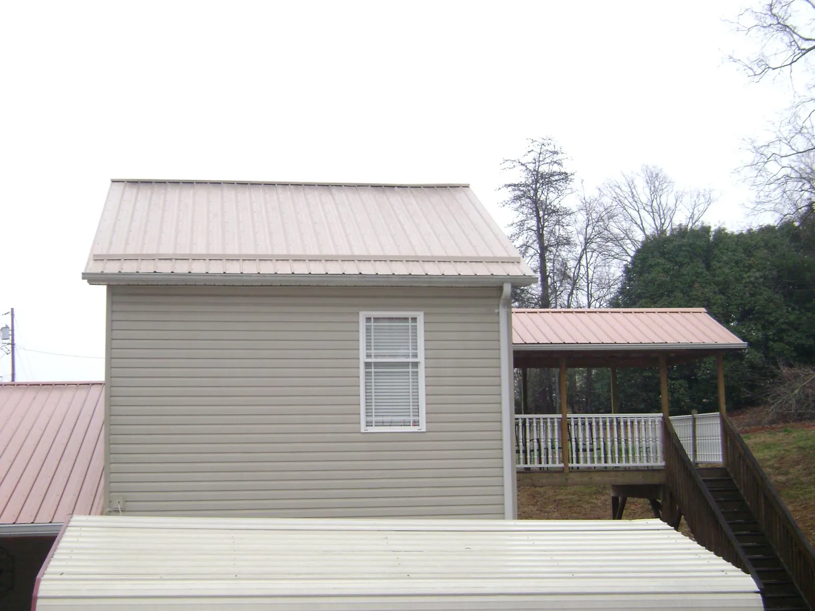Tan metal roofs on a two story addition and attached porch, from a Roof Replacement job in Iron Ridge